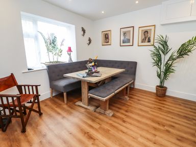 A dining area with a wooden table gray upholstered bench and corner seating plant in a basket and three framed pictures on the wall at Muscle Shoals in Seahouses