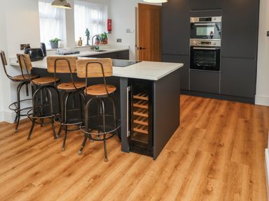 A kitchen with wooden bar stools a countertop with a sink and built in ovens at Muscle Shoals in Seahouses