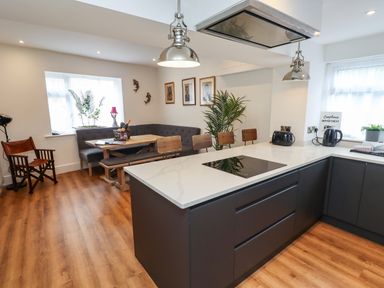 A kitchen with a white countertop island and black cabinets next to a dining area with a wooden table and bench at Muscle Shoals in Seahouses