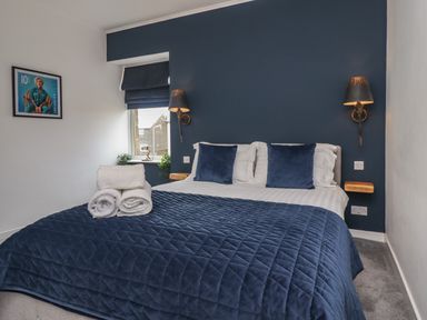 A bedroom with a bed with blue bedding and pillows two wall lamps and a window with blue blinds at Muscle Shoals in Seahouses