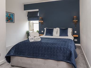 A bedroom with a double bed navy blue quilt and pillows two wall lamps and a window at Muscle Shoals in Seahouses