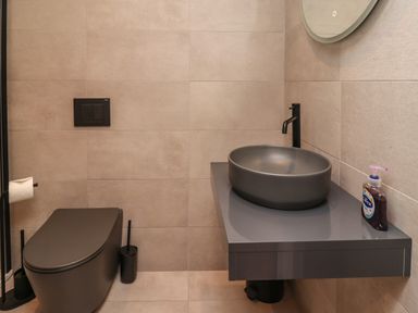 A bathroom with a gray toilet and a gray sink with a black faucet and liquid soap at Muscle Shoals in Seahouses
