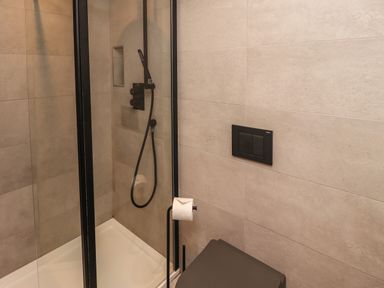 A bathroom with a walk-in shower with black fixtures and a gray toilet at Muscle Shoals in Seahouses