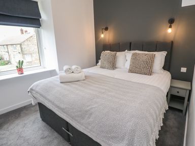 A bedroom with a double bed two pillows bedside tables and a window with a cactus plant at Muscle Shoals in Seahouses