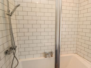 A bathroom with a bathtub a showerhead and white tiled walls at Muscle Shoals in Seahouses