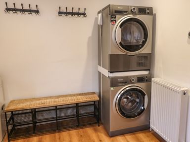 A laundry room with stacked washer and dryer a bench with storage baskets coat hooks and a radiator at Muscle Shoals in Seahouses