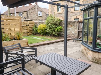 A patio with metal chairs and a table next to a garden with plants and a stone house at Muscle Shoals in Seahouses