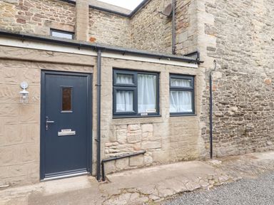 Exterior stone wall with a dark door and two windows with white curtains at Muscle Shoals in Seahouses