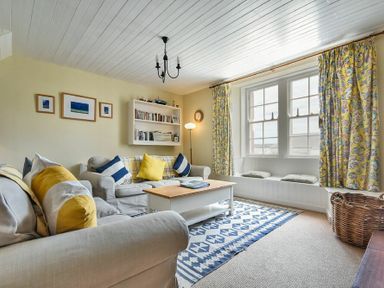 A living room with sofas, cushions, a coffee table, bookshelf, window seat, and patterned curtains at Sandpiper Cottage Low Newton-by-the-Sea
