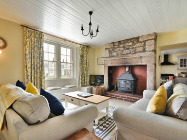A living room with two sofas a wooden coffee table a fireplace and floral curtains at Sandpiper Cottage Low Newton-by-the-Sea