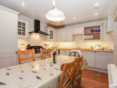 A kitchen with a wooden dining table and chairs a stove sink and cabinets at Sandpiper Cottage Low Newton-by-the-Sea
