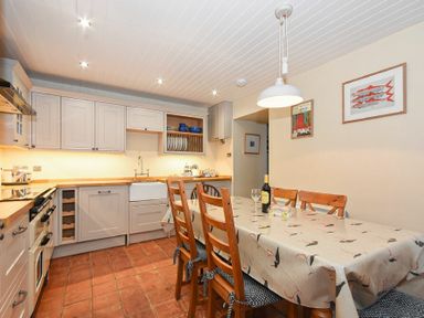 A kitchen with wooden cabinets dining table with six chairs a wine bottle and glass on table at Sandpiper Cottage Low Newton-by-the-Sea