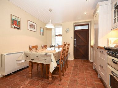 A kitchen with a dining table and chairs a wooden door and tiled floor at Sandpiper Cottage Low Newton-by-the-Sea