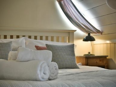 A bed with patterned pillows and rolled white towels with a wooden nightstand and lamp at Sandpiper Cottage Low Newton-by-the-Sea