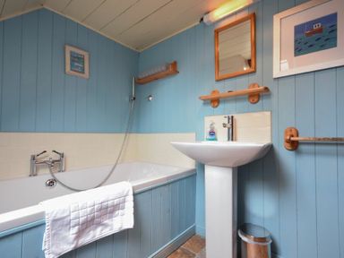 A bathroom with a bathtub sink mirror towel and trash bin at Sandpiper Cottage Low Newton-by-the-Sea