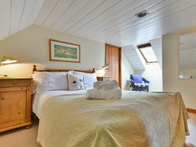 A bedroom with a bed with rolled towels bedside tables wooden door and a chair by a skylight window at Sandpiper Cottage Low Newton-by-the-Sea