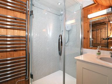 A bathroom with a glass shower enclosure a sink with a countertop and a mirror mounted on a wooden wall at Sandpiper Cottage Low Newton-by-the-Sea