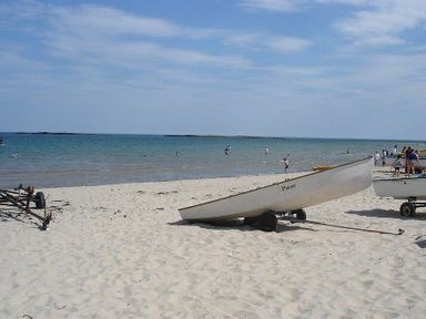 White sand beach with small boats on trailers and people in the water at Sandpiper Cottage Low Newton-by-the-Sea