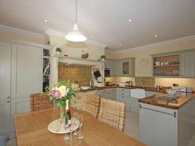 A kitchen with wooden table and woven chairs and cabinets with a clock on the wall at Grange Cottage in Alnmouth