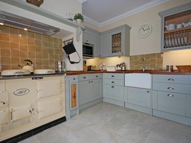 A kitchen with light gray cabinets wooden countertops a cream stove and a wall clock at Grange Cottage in Alnmouth