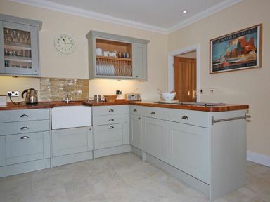 A kitchen with grey cabinets wooden countertops a white sink clock on the wall and a Bamburgh poster at Grange Cottage in Alnmouth