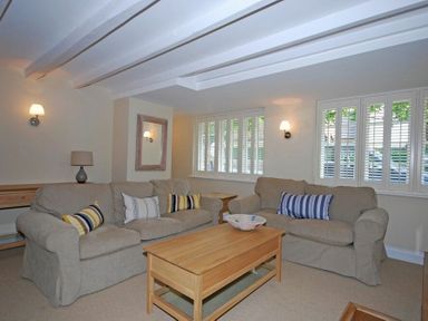 A living room with two sofas a wooden coffee table and white shuttered windows at Grange Cottage in Alnmouth