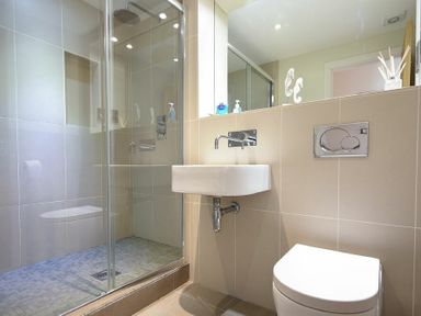 A bathroom with a shower cabin a wall-mounted sink and a toilet at Grange Cottage in Alnmouth