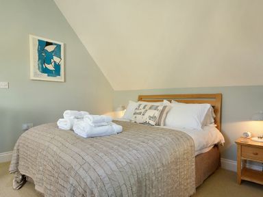 A bedroom with a bed with pillows and folded towels and a wooden bedside table with a lamp at Grange Cottage in Alnmouth