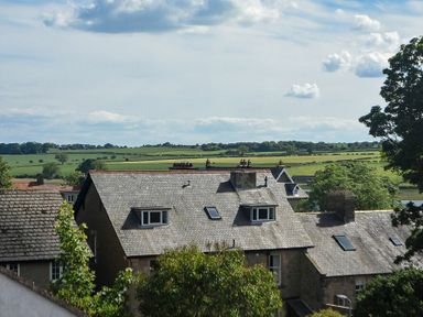 Roofs of stone houses with skylights and chimneys with green fields and trees in the background at Grange Cottage in Alnmouth