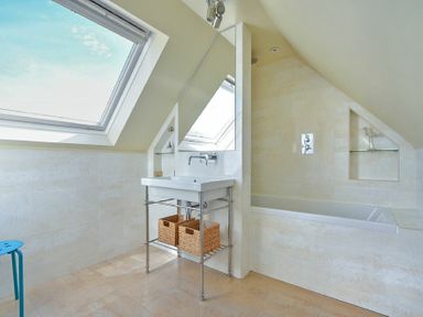 A bathroom with a white sink on a metal stand and a built in bathtub under a slanted ceiling at Grange Cottage in Alnmouth