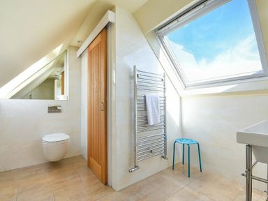 A bathroom with a wall-mounted toilet wooden door metal towel rack blue stool and large skylight window at Grange Cottage in Alnmouth