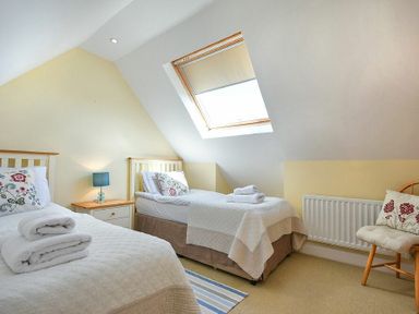 A bedroom with two single beds bedside table with lamp skylight window and a wooden chair with cushions at Grange Cottage in Alnmouth