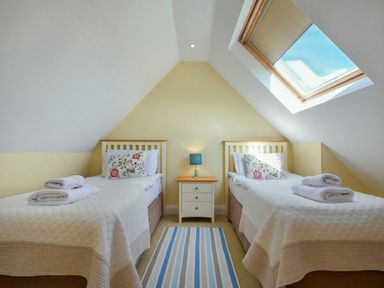 A bedroom with two single beds a nightstand with a blue lamp and a skylight window at Grange Cottage in Alnmouth