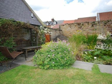 A garden with a wooden bench and chair near stone wall and plants at Grange Cottage in Alnmouth