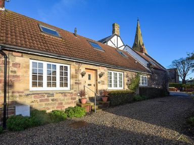 A stone house with white-framed windows and a red tiled roof under a clear blue sky at Grange Cottage in Alnmouth