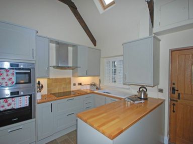 A kitchen with wooden countertops gray cabinets a stove a kettle and an oven at Martins Cottage in Alnmouth