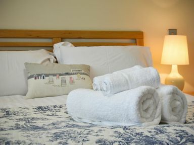 A bed with white pillows and rolled white towels with a lamp on a bedside table at Martins Cottage in Alnmouth
