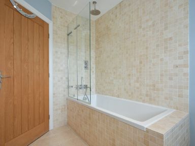 A bathroom with a bathtub and shower and wooden door at Martins Cottage in Alnmouth
