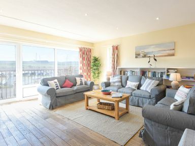 A living room with three gray sofas a wooden coffee table floor lamp bookshelf and large windows with curtains at The Boathouse Alnmouth