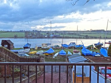 A view of boats on land near a body of water with green fields and trees in the background at The Boathouse (Alnmouth) in Alnmouth