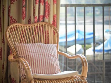 A rattan chair with cushions next to window with curtain showing boats outside at The Boathouse (Alnmouth) in Alnmouth