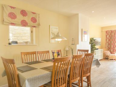 A dining room with a table and wooden chairs near a window with floral curtains at The Boathouse (Alnmouth) in Alnmouth