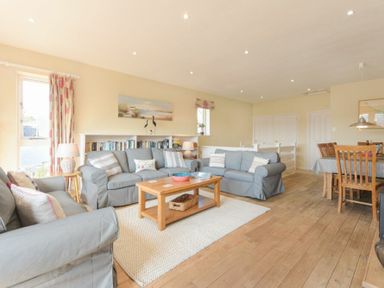 A living room with grey sofas a wooden coffee table and a dining table with chairs at The Boathouse (Alnmouth) in Alnmouth