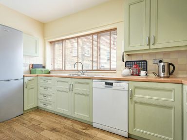 A kitchen with green cabinets a dishwasher a refrigerator and wooden flooring at The Boathouse (Alnmouth) in Alnmouth