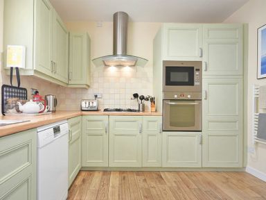 A kitchen with green cabinets wooden floor and stainless steel appliances at The Boathouse (Alnmouth) in Alnmouth