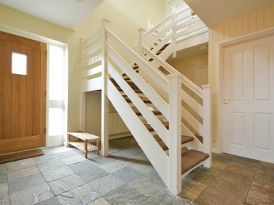An entryway with a wooden front door, tiled floor, white staircase, and a small wooden bench at The Boathouse (Alnmouth) in Alnmouth
