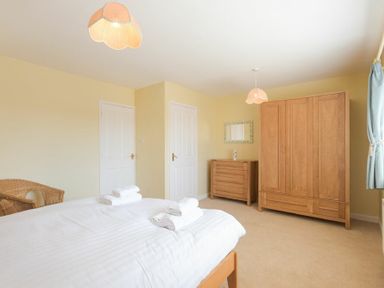 A bedroom with a bed with folded towels a wardrobe a chest of drawers and a wicker chair at The Boathouse (Alnmouth) in Alnmouth