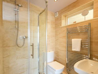 A bathroom with a glass shower enclosure a toilet a heated towel rail and a window at The Boathouse (Alnmouth) in Alnmouth