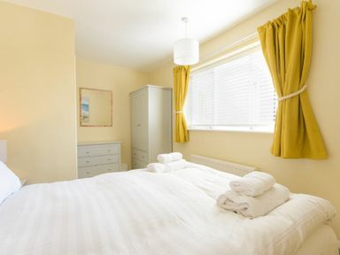 A bedroom with a bed holding folded towels a dresser a wardrobe and yellow curtains at The Boathouse in Alnmouth
