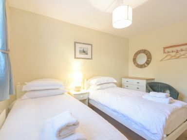 A bedroom with two single beds white linens bedside table with lamp dresser and mirror at The Boathouse (Alnmouth) in Alnmouth